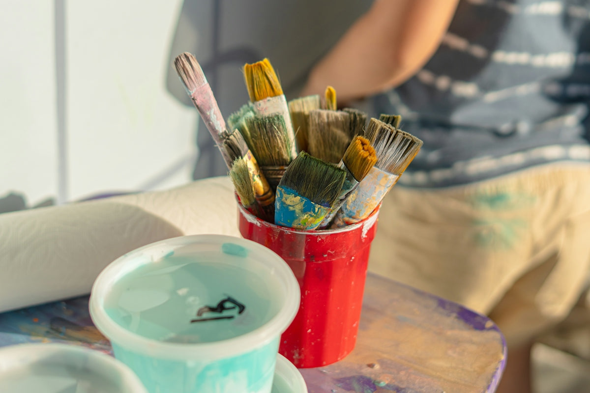 Paintbrushes rest in a red cup with paint cups