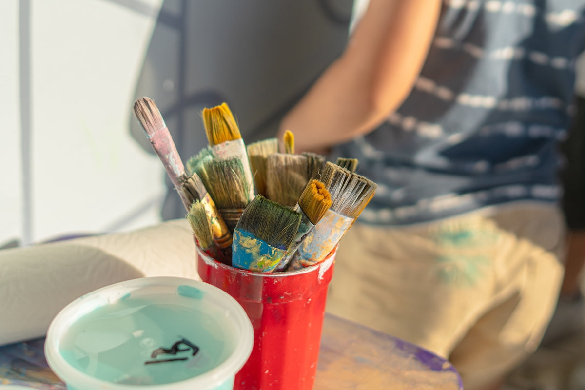 Paintbrushes in a cup sit on a table.