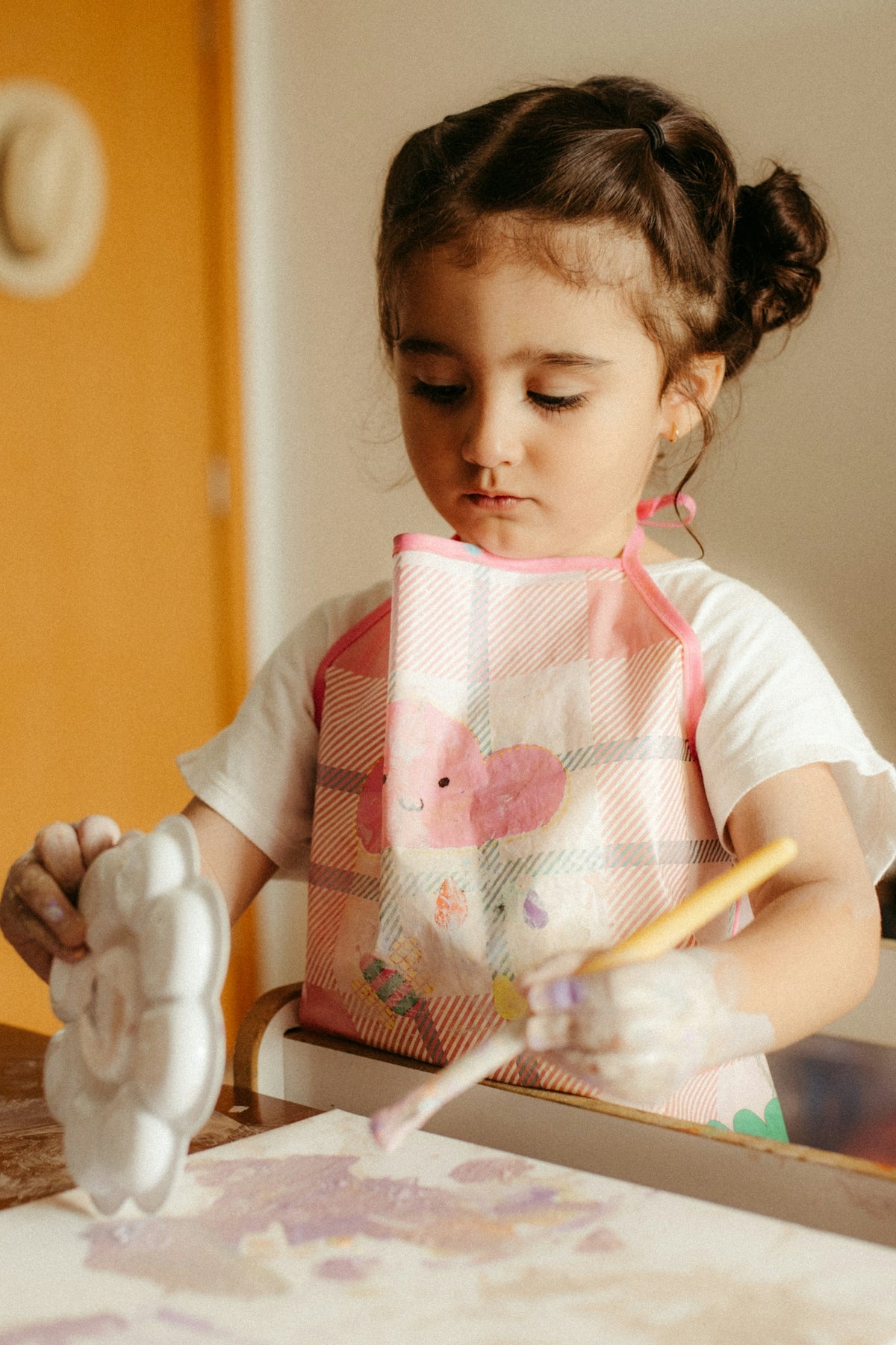 Young girl painting with purple paint at a table.
