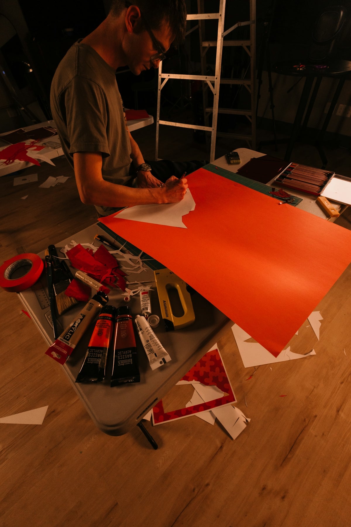 Man cutting orange paper with scissors at a table.
