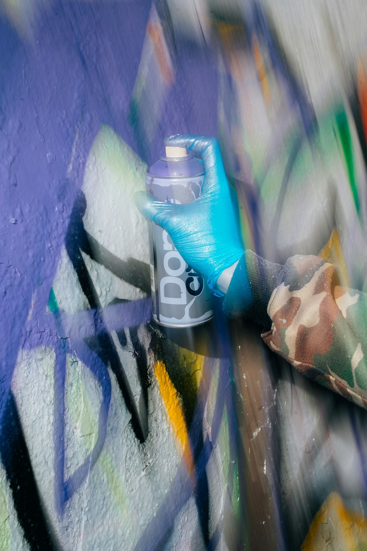 Hand in blue glove spraying purple paint on wall.