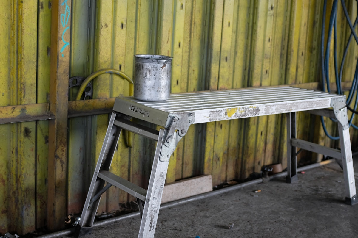 a metal step stool sitting next to a wooden wall