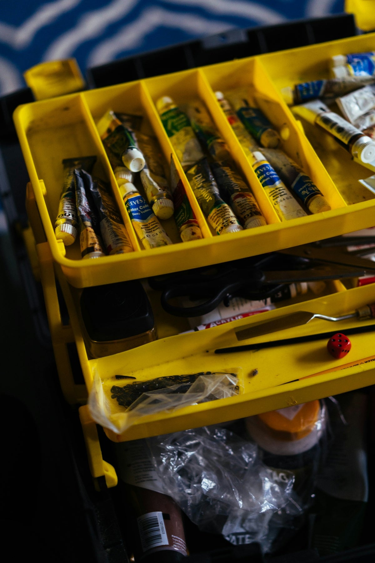 A yellow tiered art supply organizer filled with paint tubes and tools